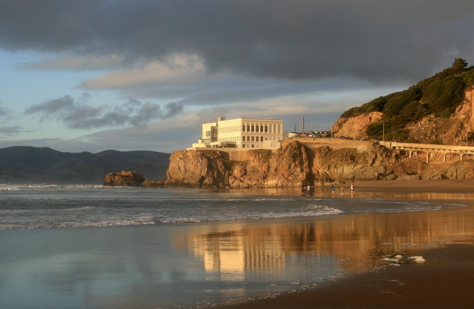 A beach with a building on a cliff overlooking the ocean.
