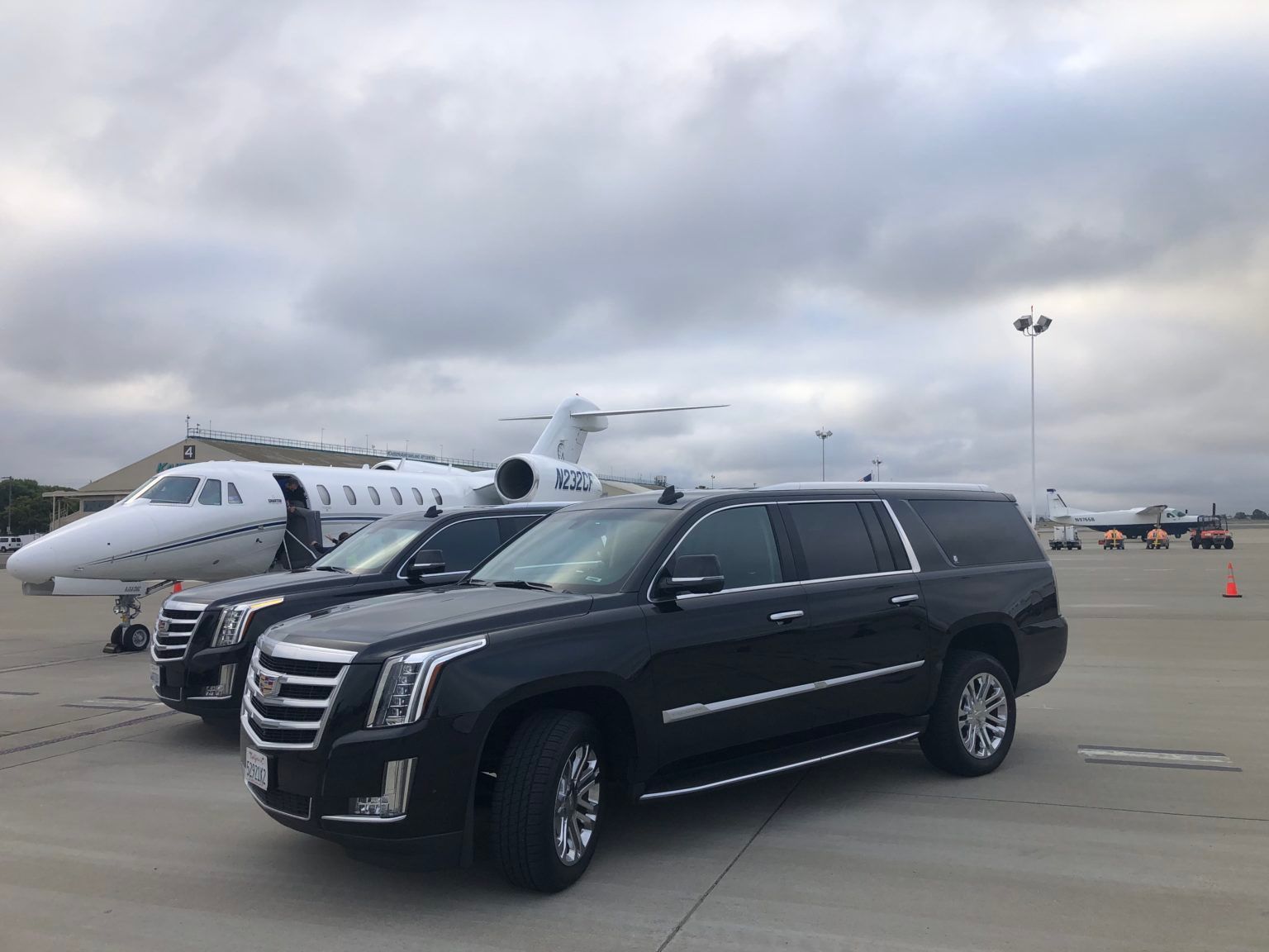 A row of cars are parked next to a jet on a runway.