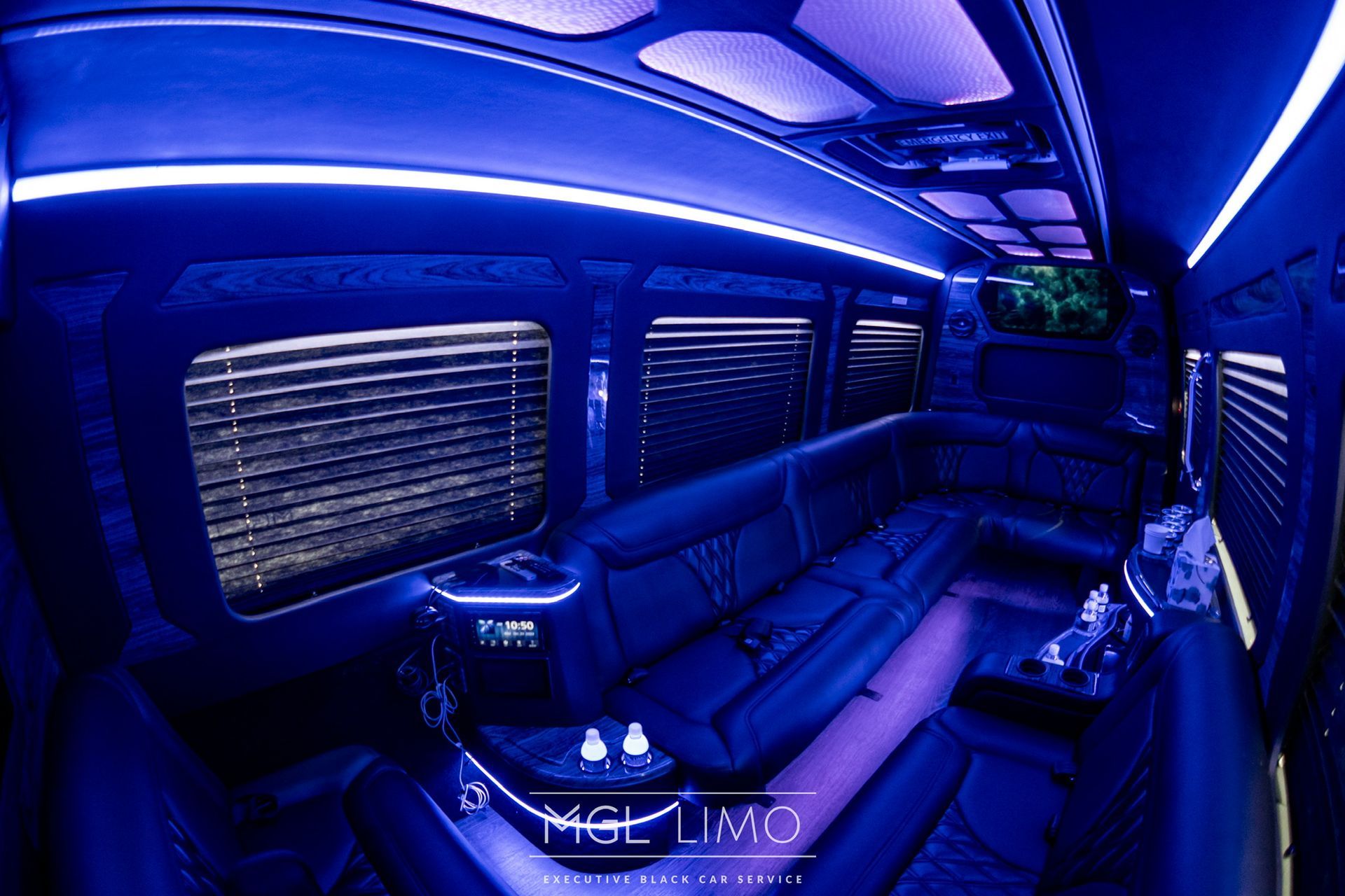 Inside of a black limousine with blue interior lighting. Seats line both sides with a bar.