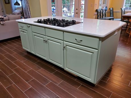Kitchen island with a light green cabinet base, white countertop, and built-in stovetop. 