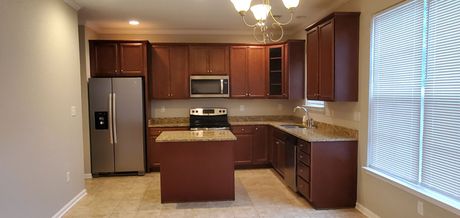 A kitchen featuring dark brown cabinetry, a stainless steel refrigerator, a center island, and granite countertops.