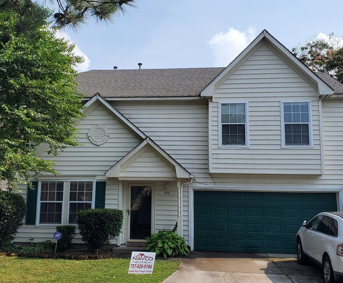 Two-story white house with a dark green garage door. Green shutters and landscaping, with a white car parked in front.