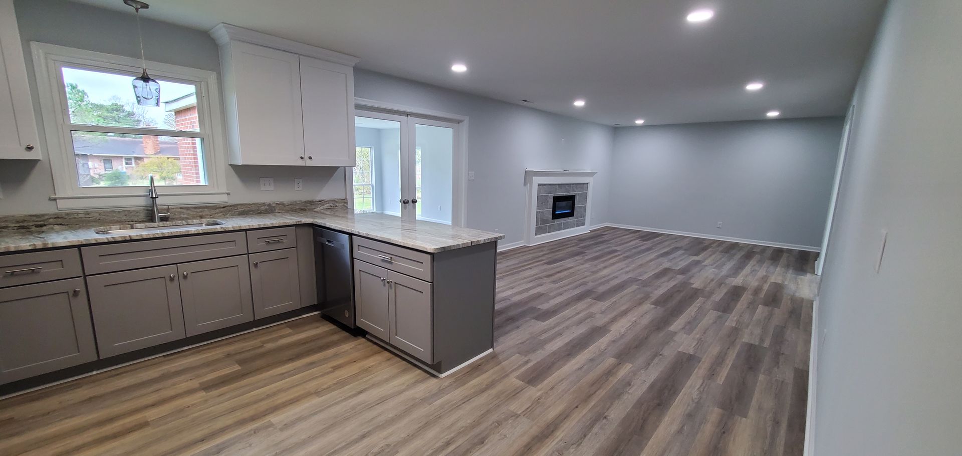 Newly renovated kitchen and living room with gray and white cabinets, light gray walls, and wood-look flooring. 