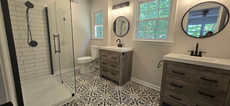 Bathroom with patterned tile floor, two vanities with round mirrors, a shower with black trim, and a toilet.