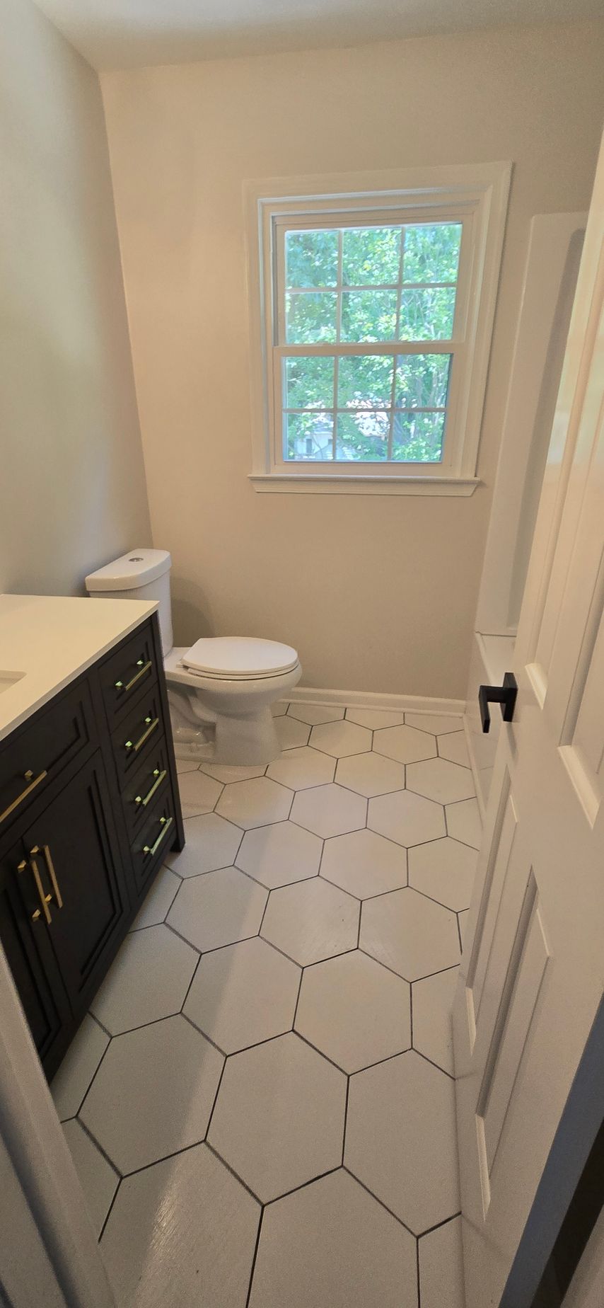 A small bathroom featuring white hexagon tile floors with black grout. The room has a white toilet.
