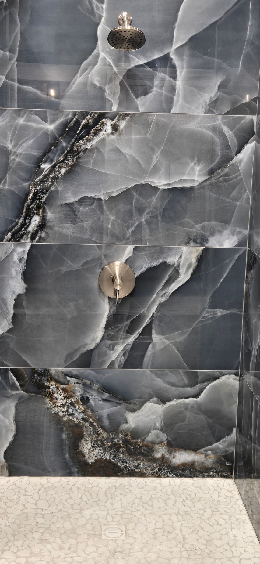 Shower with dark blue marble-like tiles and silver fixtures. Light-colored textured floor.