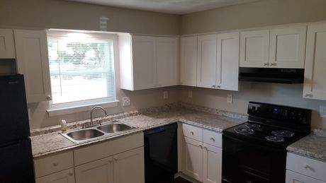 White kitchen with black appliances, granite countertops, and a window.