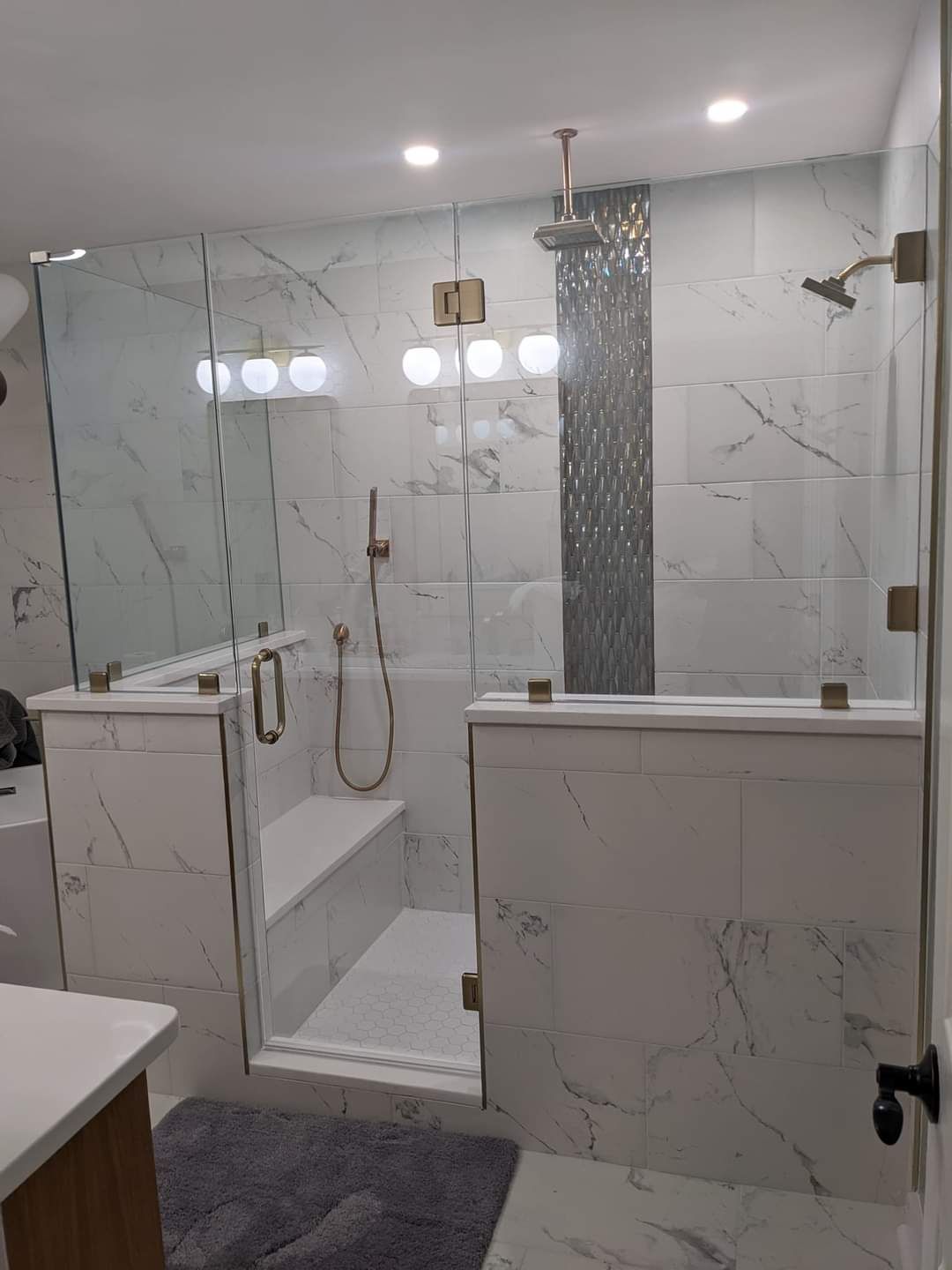 Spacious, modern bathroom with a walk-in shower. Marble tile, glass walls, and gold fixtures create a luxurious look.