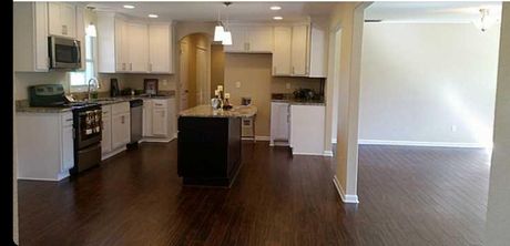 A modern kitchen with white cabinets, dark wood floors, and a black island, leading into an open living space.