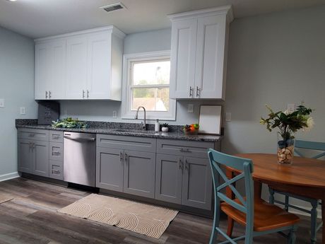 A modern kitchen with gray and white cabinets, granite countertops, and a wooden dining table with blue chairs.