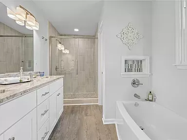 A modern bathroom with a white bathtub, shower, and vanity. Light wood-look flooring and gray-toned tile in the shower.