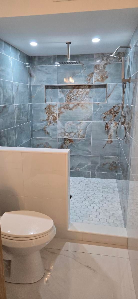 A bathroom featuring a walk-in shower with gray and brown tile, a white toilet.