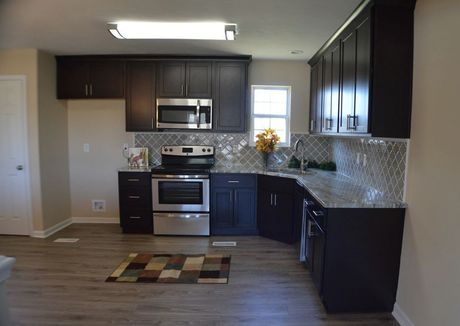 Dark-cabinet kitchen with stainless steel appliances and a stone backsplash. 