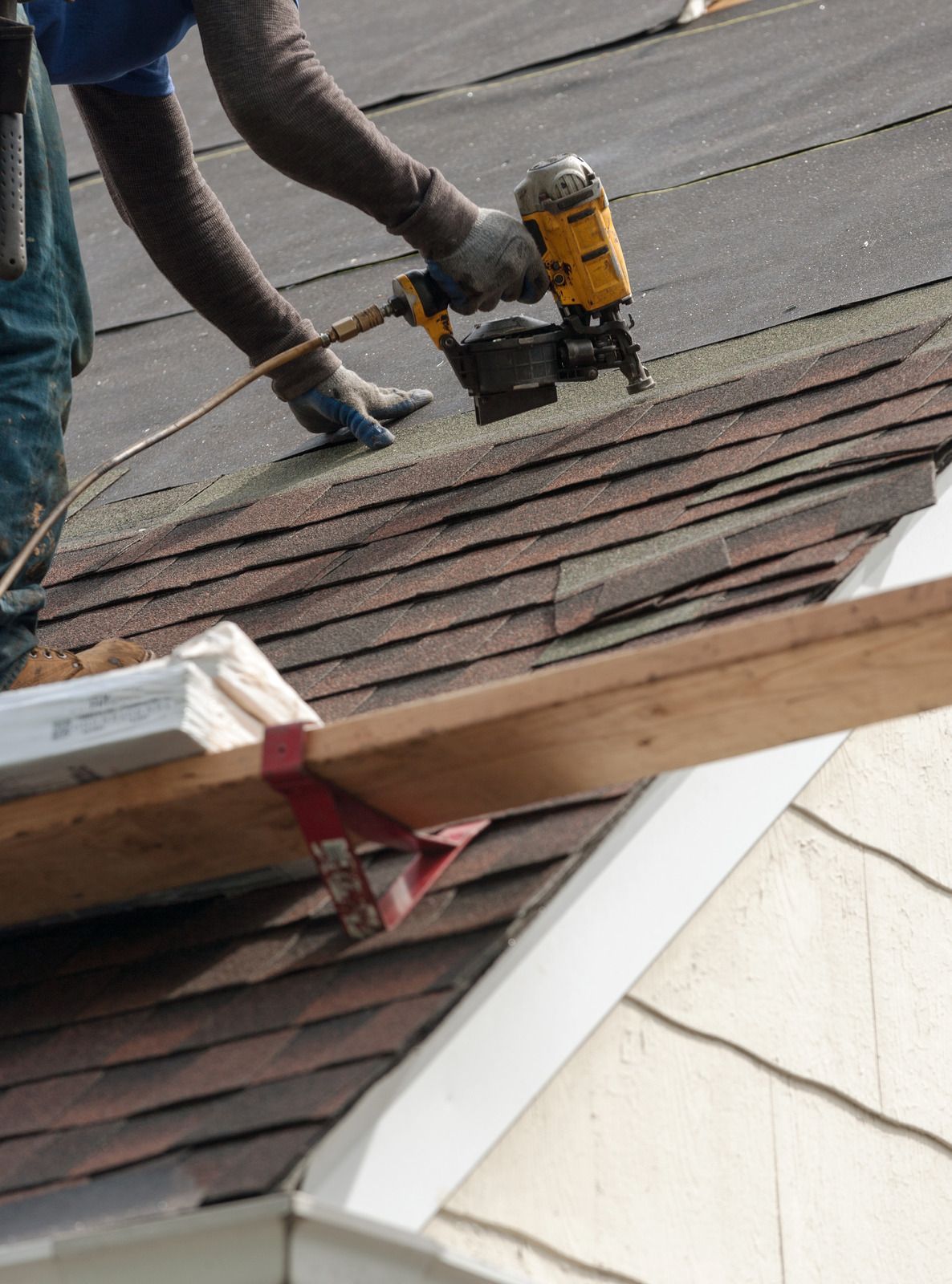 A person digs a trench in a backyard near a small excavator, a tree, and a house.