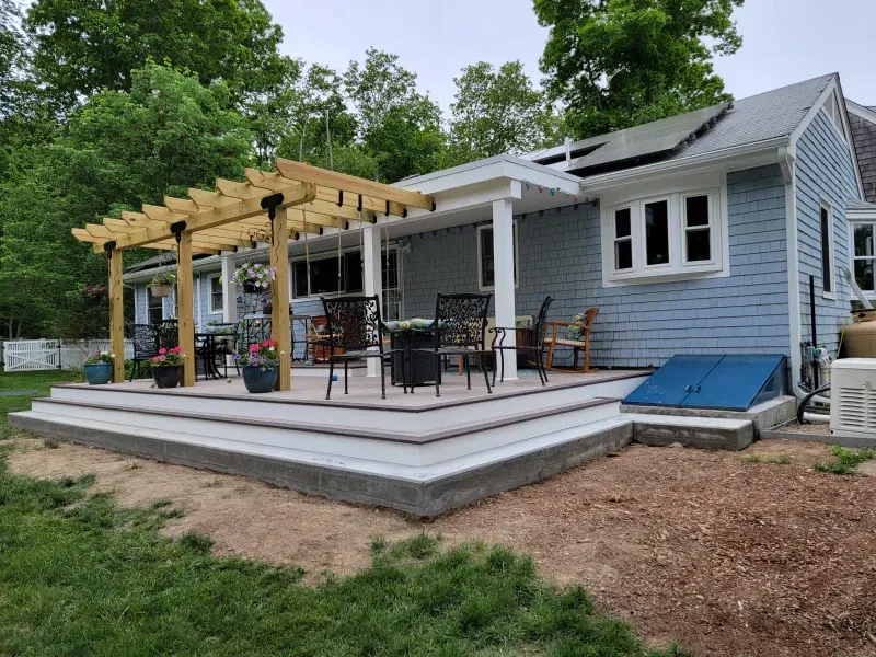 A light blue house with a wooden pergola, deck, and concrete steps in a yard.