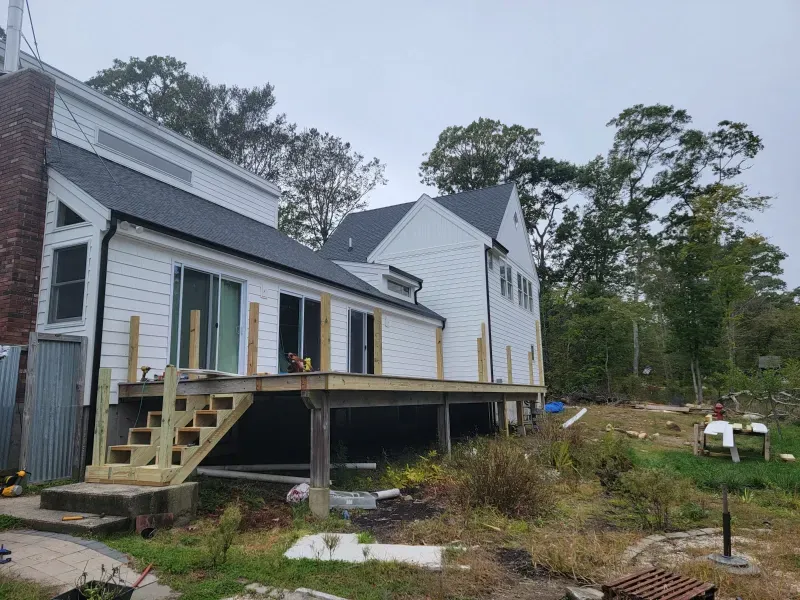 Side view of a house under construction with a new wooden deck and stairs; overcast sky.