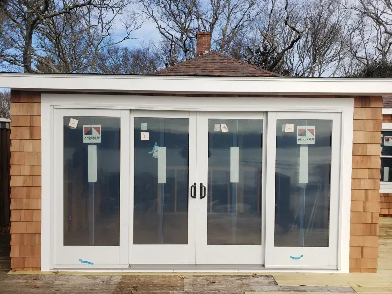 Exterior of a building with cedar shingles, white-framed glass sliding doors, and a small brown roof.