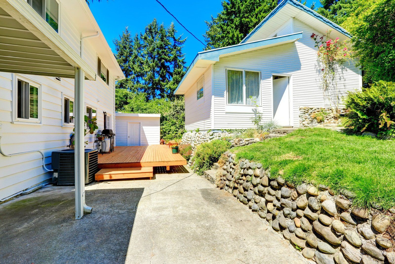 A person digs a trench in a backyard near a small excavator, a tree, and a house.