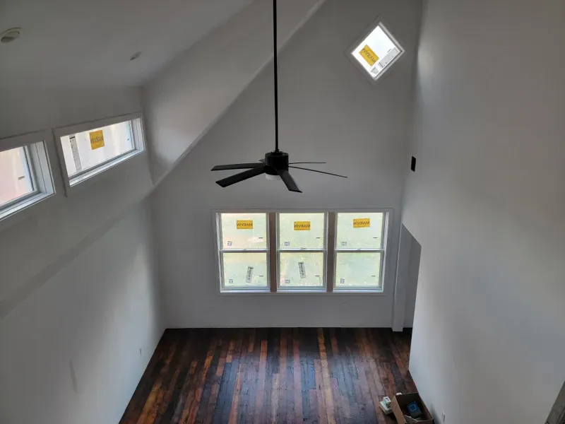 A person digs a trench in a backyard near a small excavator, a tree, and a house.