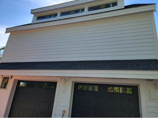 White two-story building with black garage doors, white siding, and a row of windows at the top.
