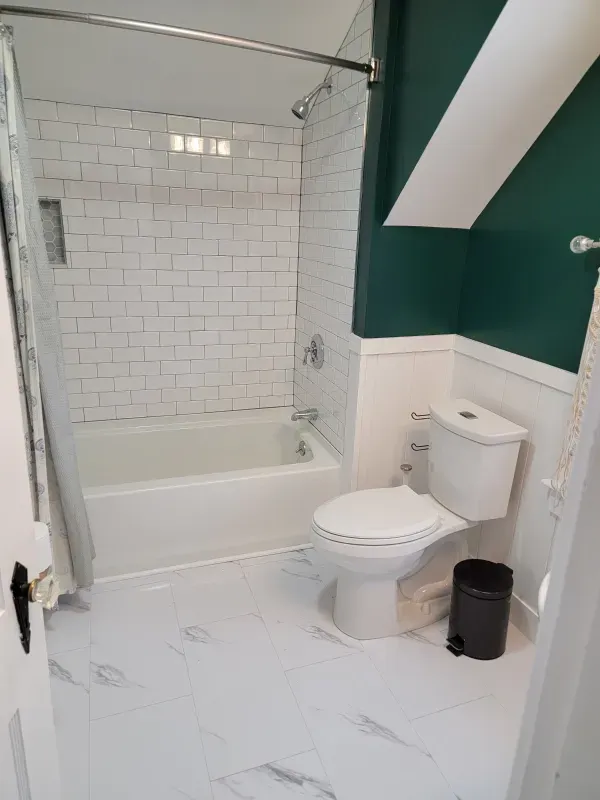 A person digs a trench in a backyard near a small excavator, a tree, and a house.