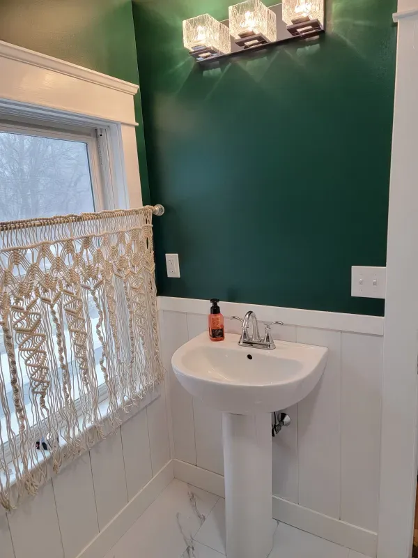 Small bathroom with white pedestal sink, green wall, and macrame window treatment.