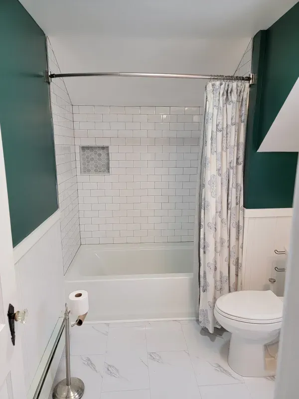 Bathroom with white subway tile shower, white tub, toilet, and marble-look floor; teal walls.