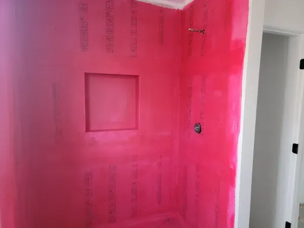Pink waterproof membrane installed in a shower, with a built-in niche and shower fixtures, ready for tile.