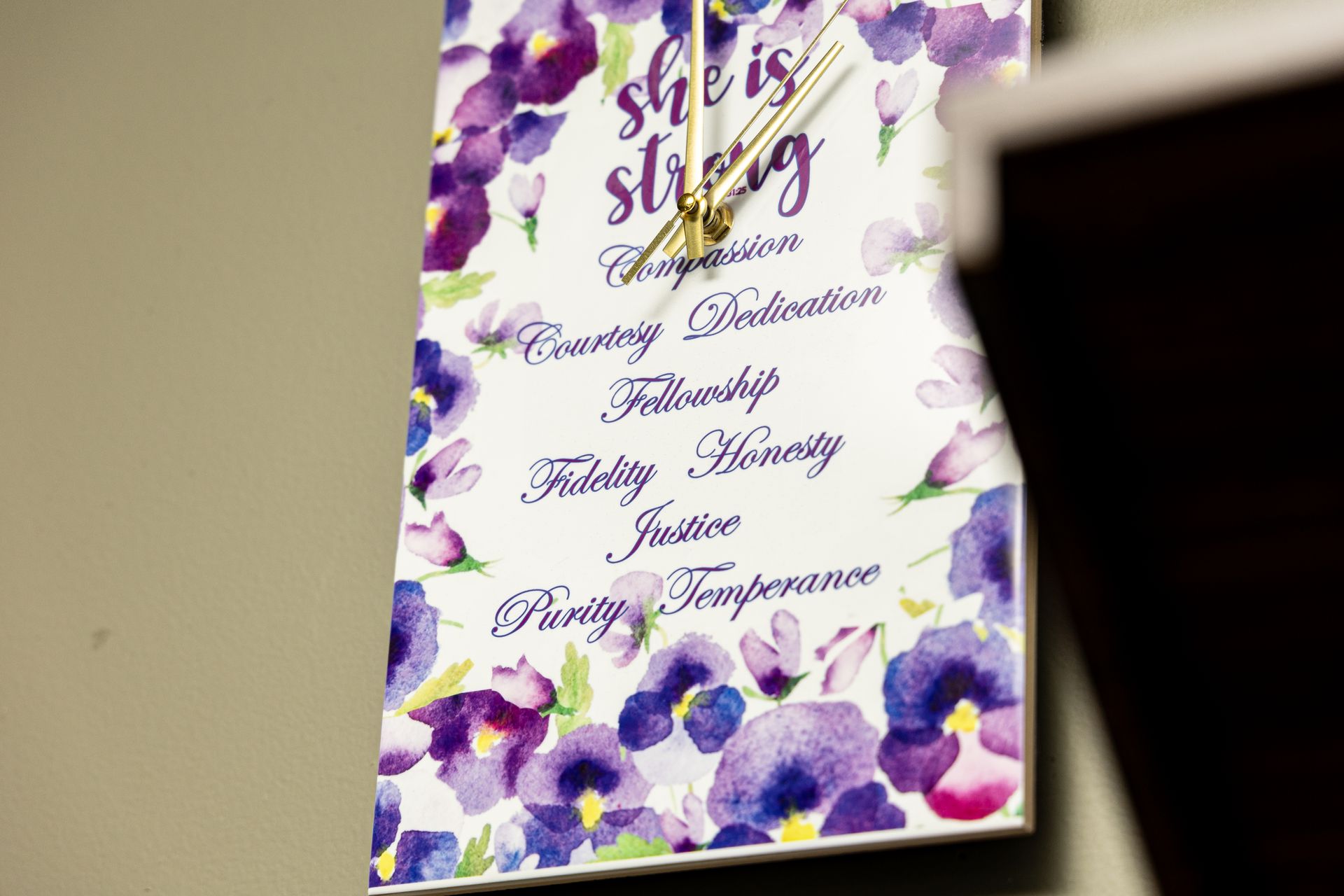 A clock with purple flowers on it that says `` she is strong ''