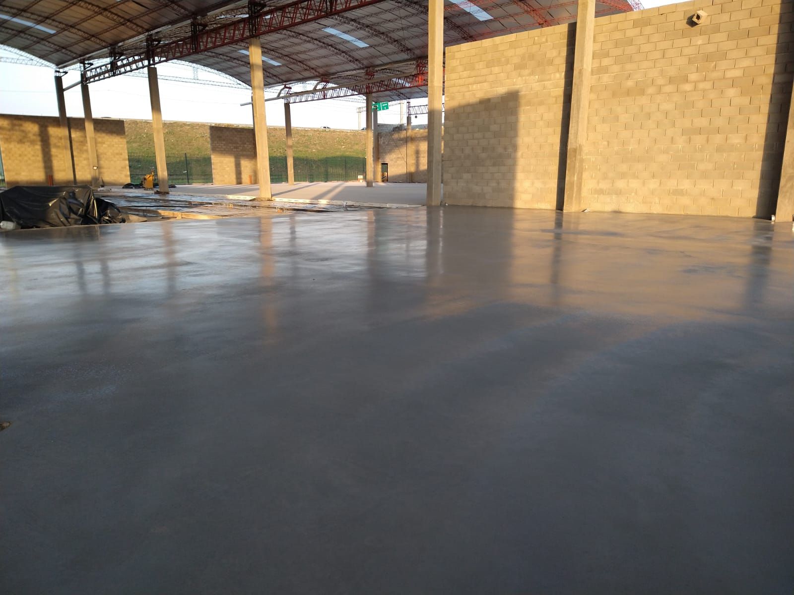 Gran edificio industrial vacío, con suelo de hormigón liso y gris, iluminado por el sol.