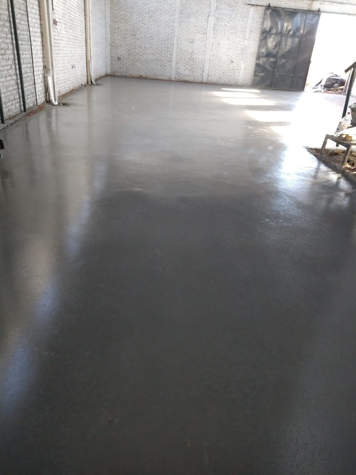 Suelo de hormigón gris brillante en un almacén. Paredes de ladrillo blanco parcialmente visibles.