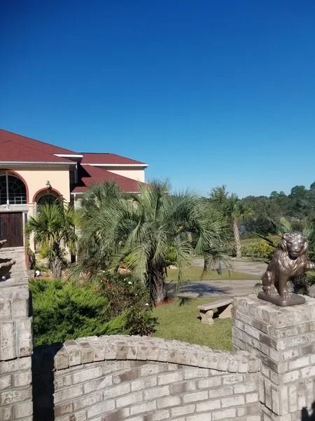 Stone wall and bronze animal statue in a landscaped garden beside a building with a red roof under a blue sky