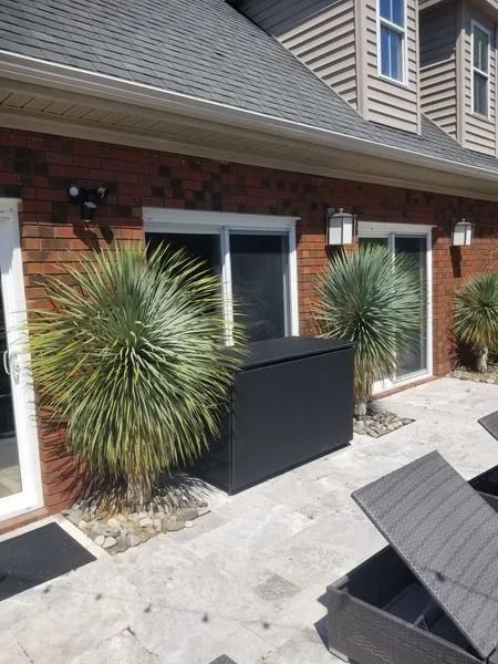 Brick house patio with two spiky shrubs and a black storage box near sliding doors