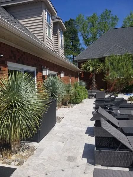 Outdoor patio beside a brick house with black lounge chairs, potted plants, and a paved walkway