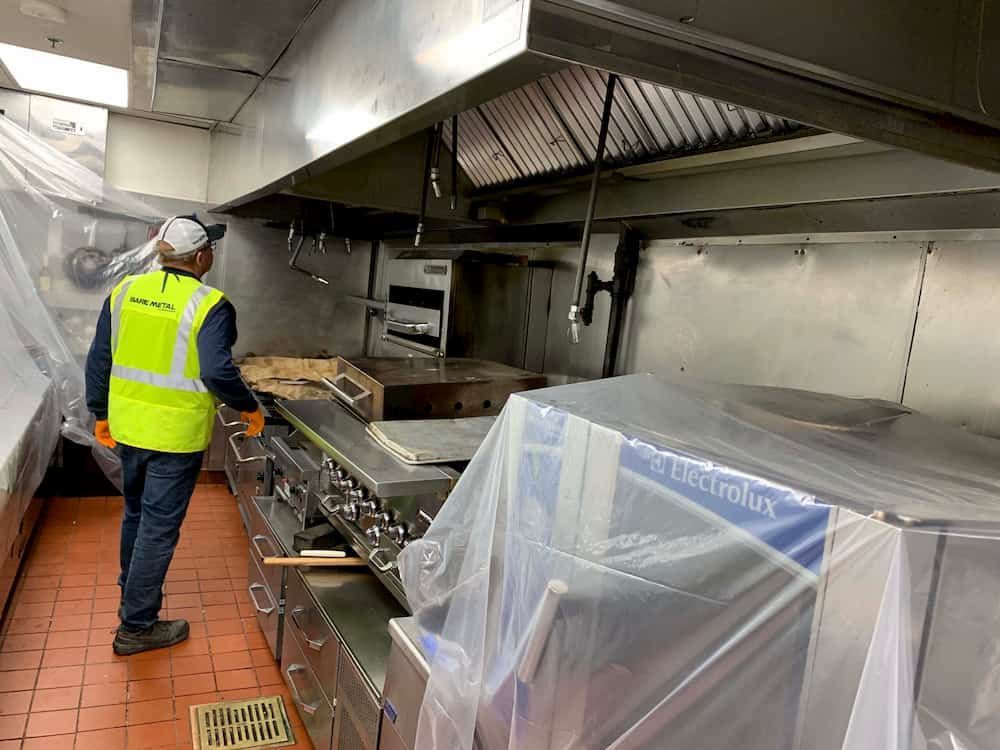 A man in a yellow vest is standing in a kitchen covered in plastic.