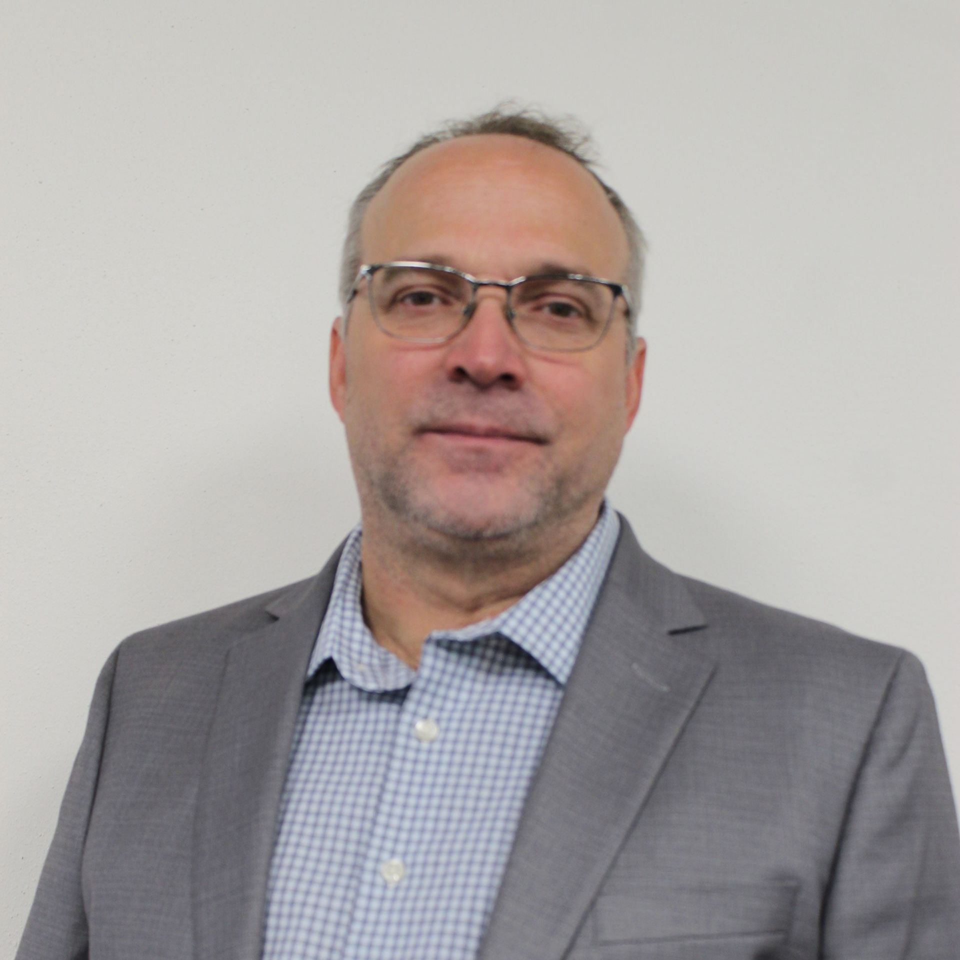 a man wearing glasses and a suit stands in front of a white wall