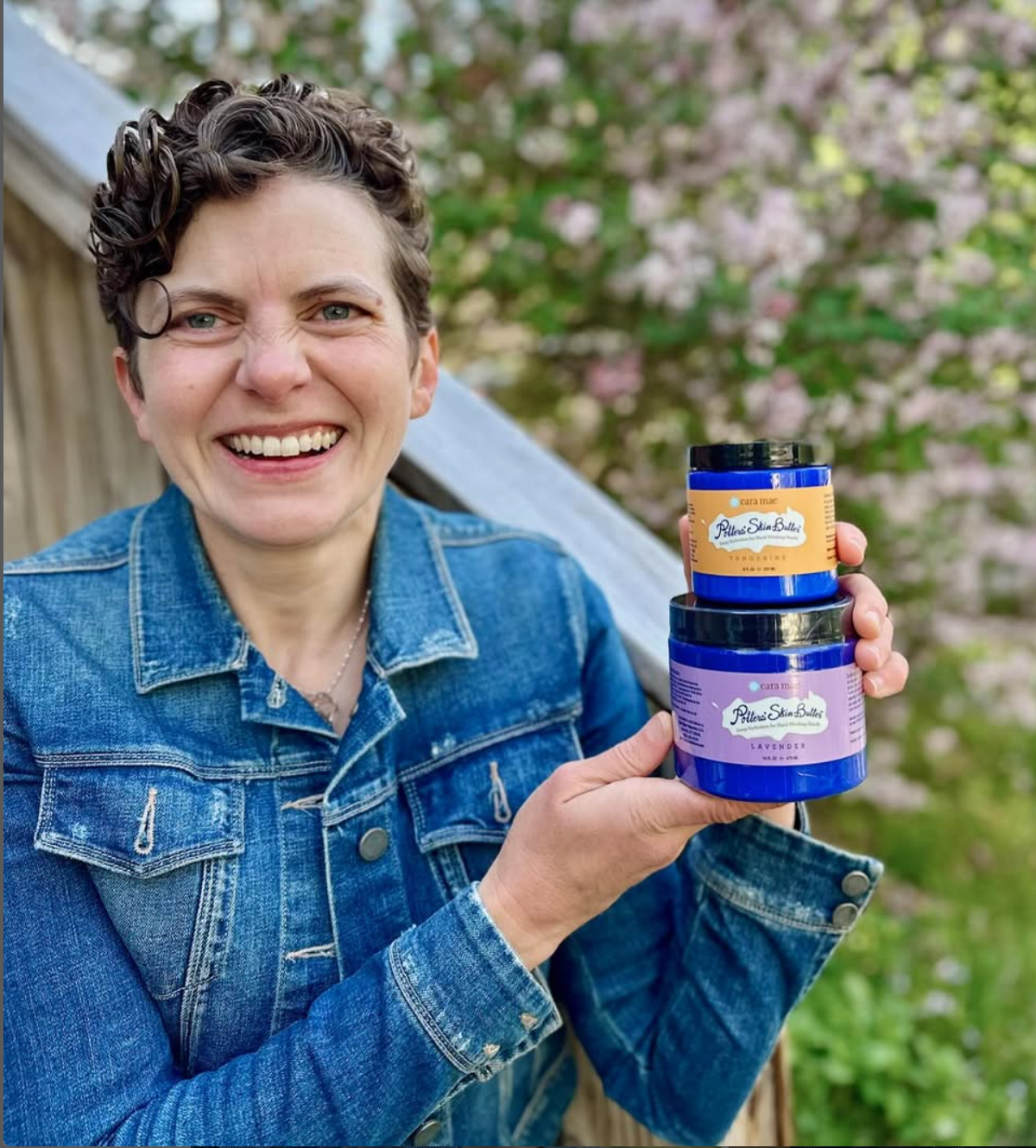 Cara Steinbuchel is wearing a denim jacket and holding two jars of Potter's Skin Butter.