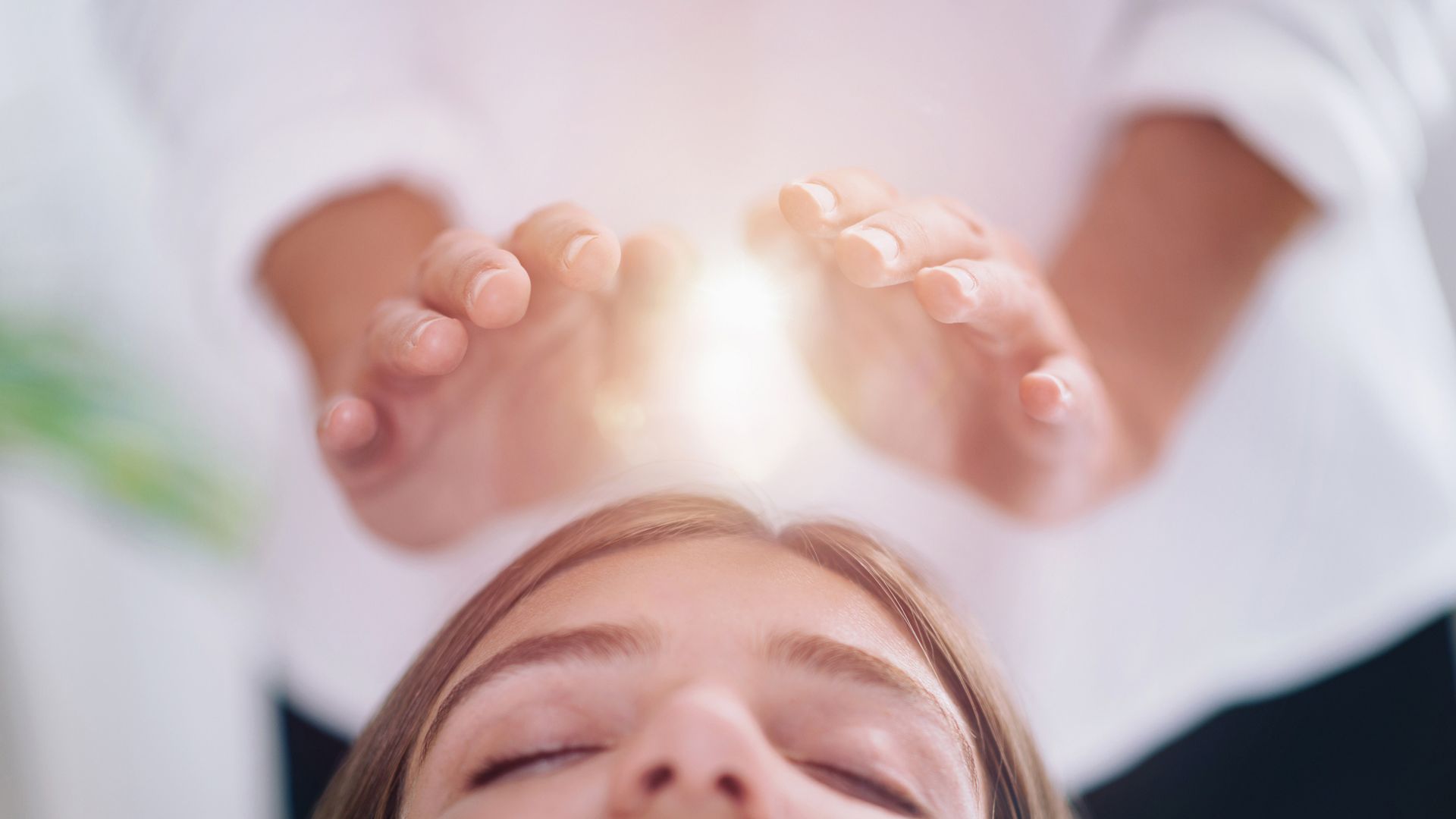 Hands above a woman's head, emitting light, suggesting energy healing.