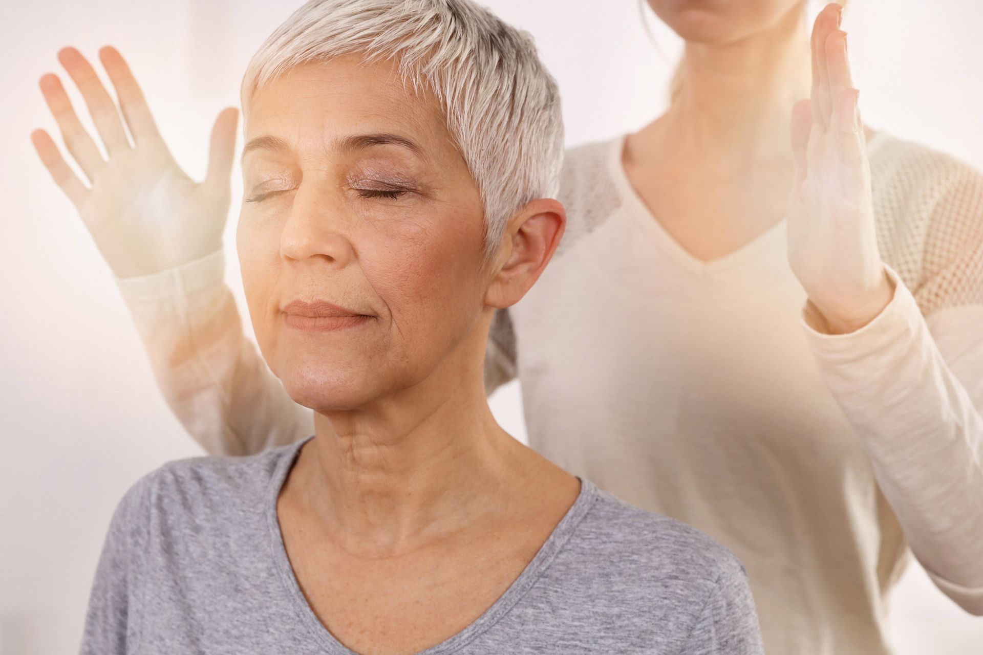 Older woman with eyes closed, receiving energy healing with hands glowing.