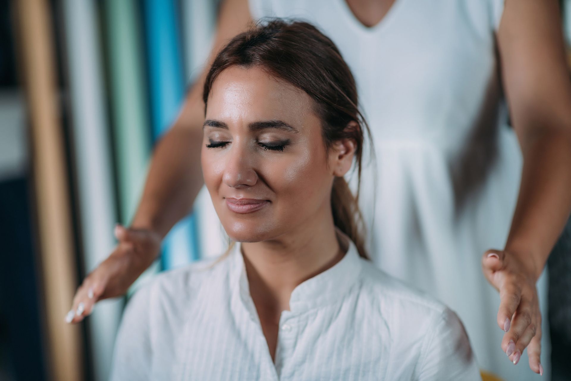 Woman receiving reiki treatment; woman with closed eyes smiles, hands held above her head.