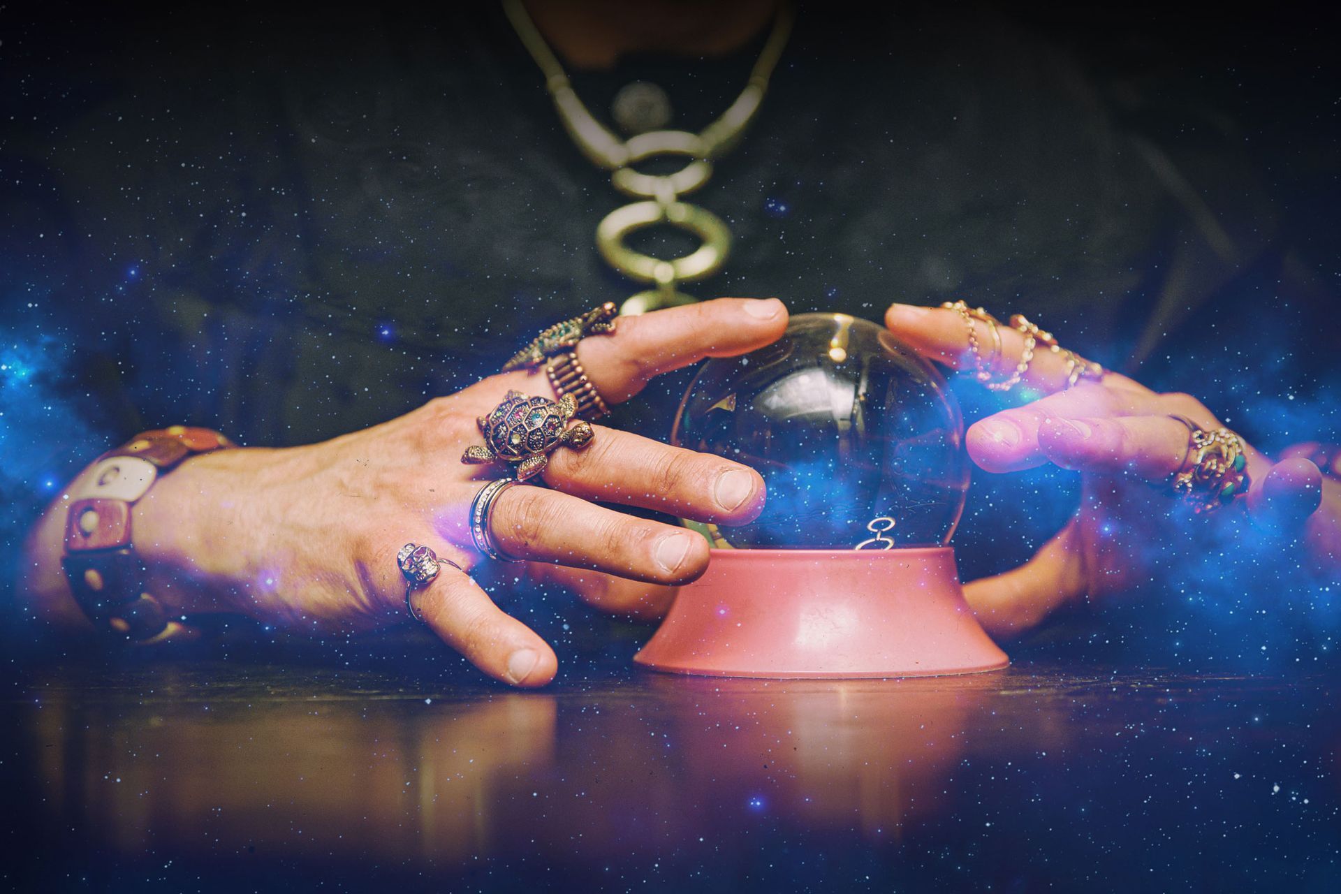 Hands adorned with rings cradle a crystal ball on a pink stand, with a dark background and starry effects.