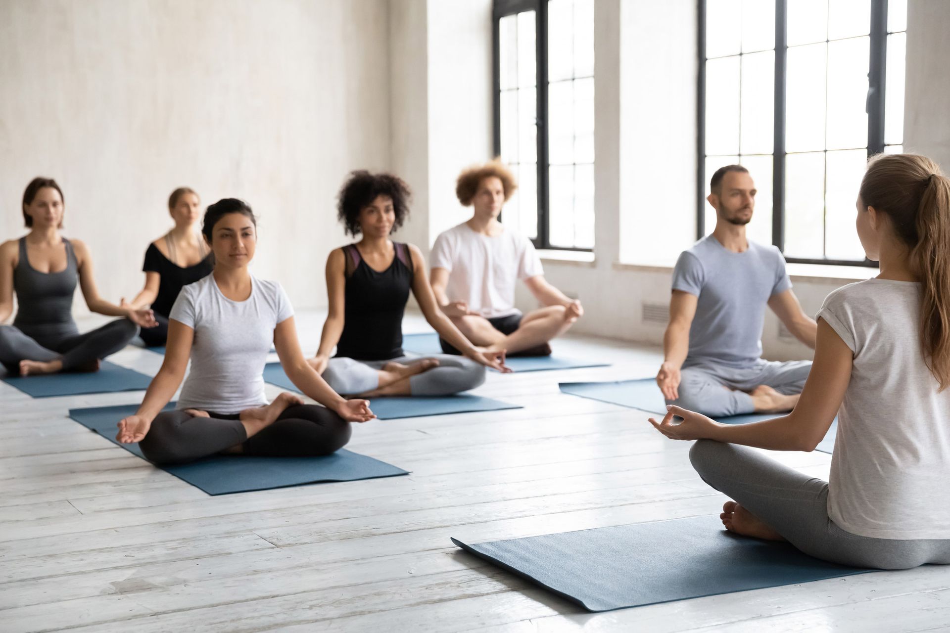Group of people in a yoga class, meditating in lotus position, led by an instructor.