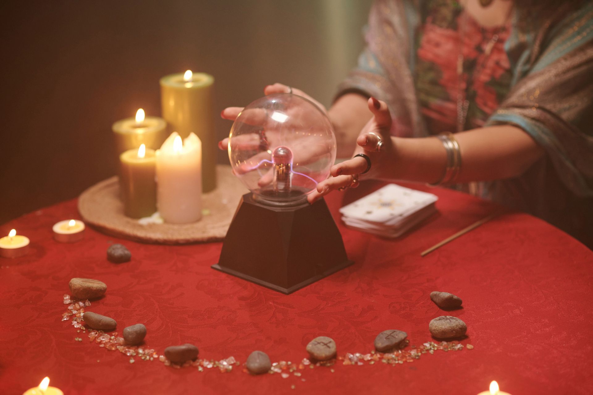 Fortune teller with hands near a crystal ball, candles, and stones on a red cloth.