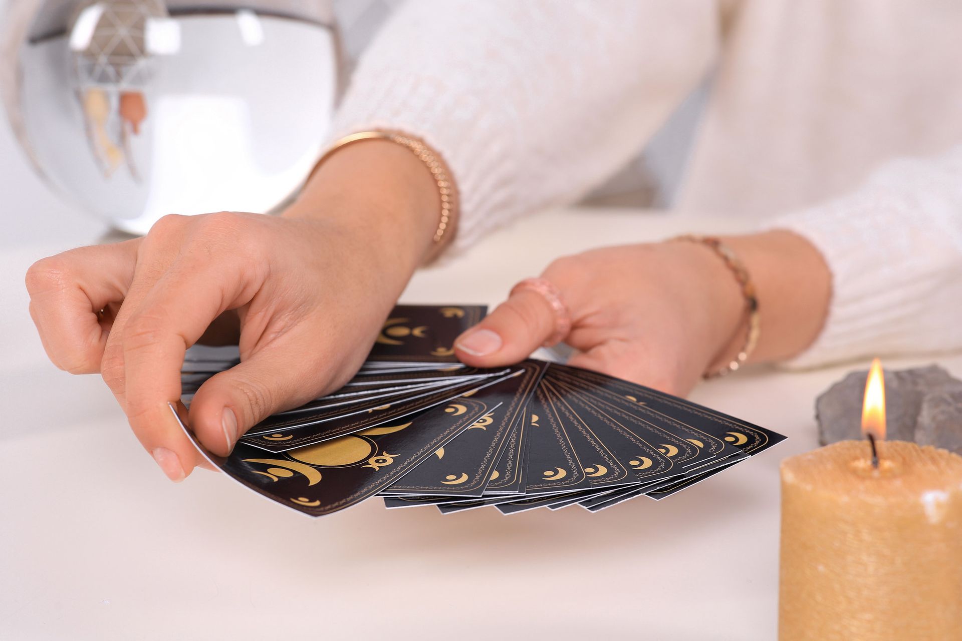 Person with hands holding tarot cards near a lit candle and a crystal ball.