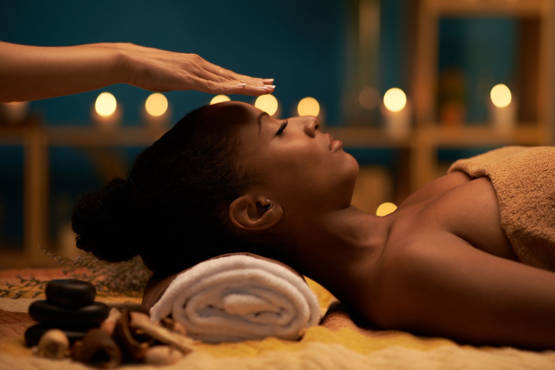 Woman receiving reiki treatment, hand above head, relaxed expression, candles in background.