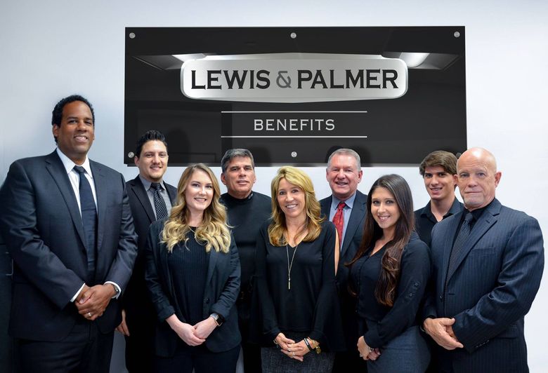 A group of people are posing for a picture in front of a sign that says lewis & palmer benefits.