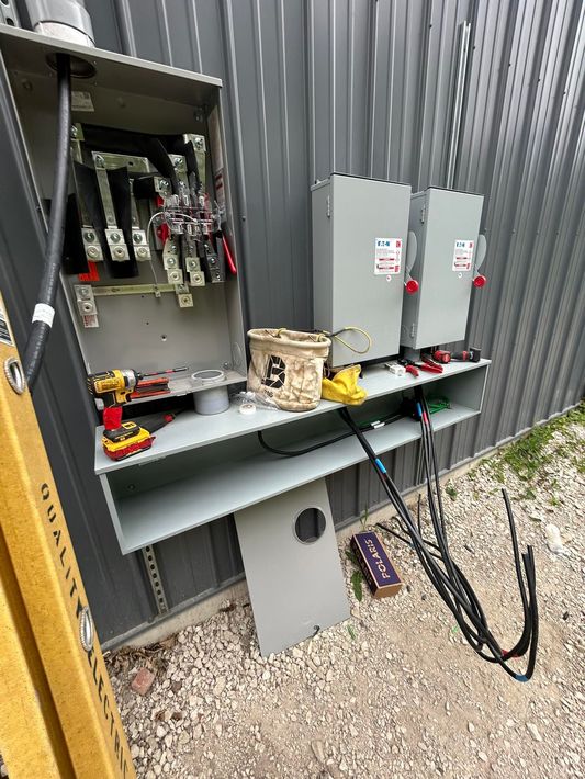 An open electrical panel and two adjacent disconnect switches mounted on a gray metal exterior wall.
