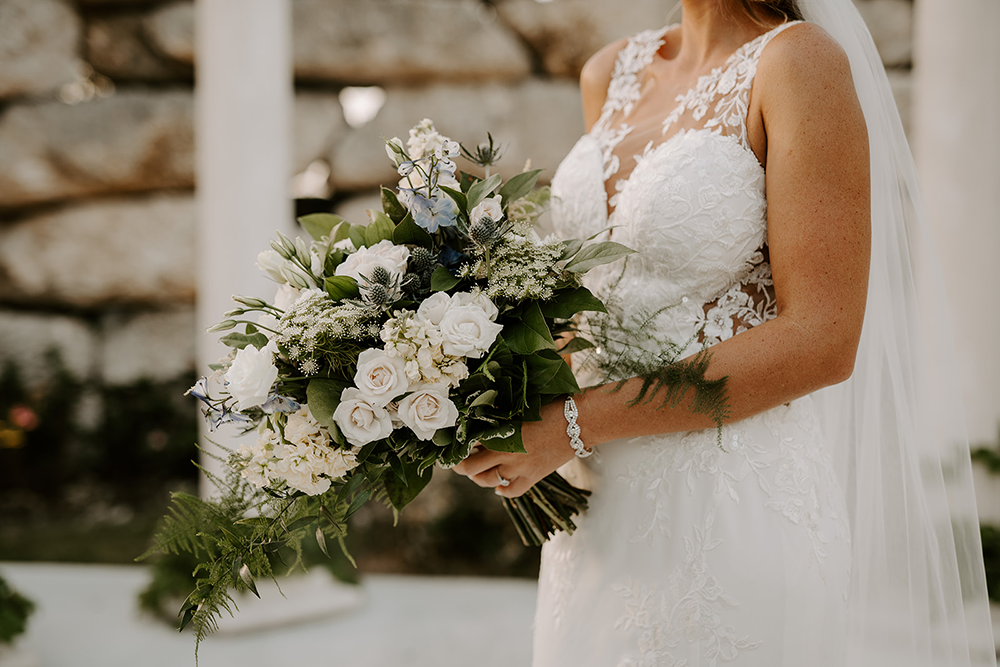 Bride in white wedding dress holding a bouquet of white and blue flowers.