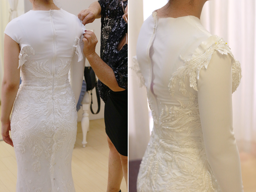 Woman in white wedding dress being fitted; seamstress adjusting sleeve.