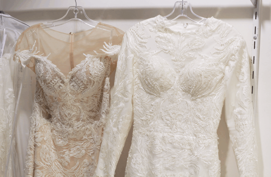 Two white wedding dresses hanging on a rack; one with long sleeves, the other sleeveless with a sheer bodice.